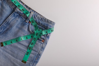 Photo of Jeans with measuring tape on light grey background, top view and space for text. Weight loss concept