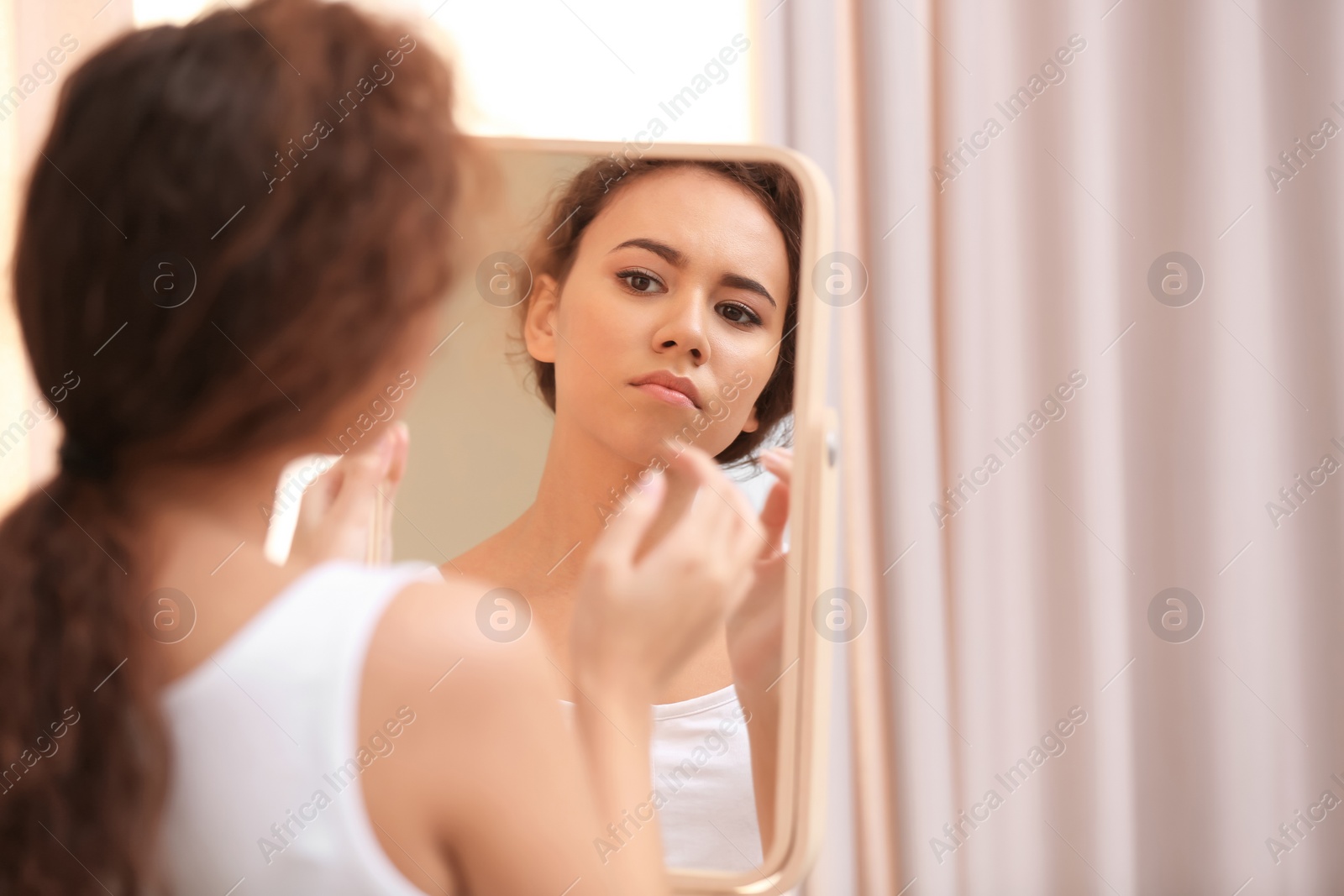 Photo of Beautiful young woman with acne problem looking in mirror at home