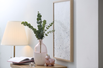 Photo of Vase with fresh eucalyptus branches on table in room. Interior design