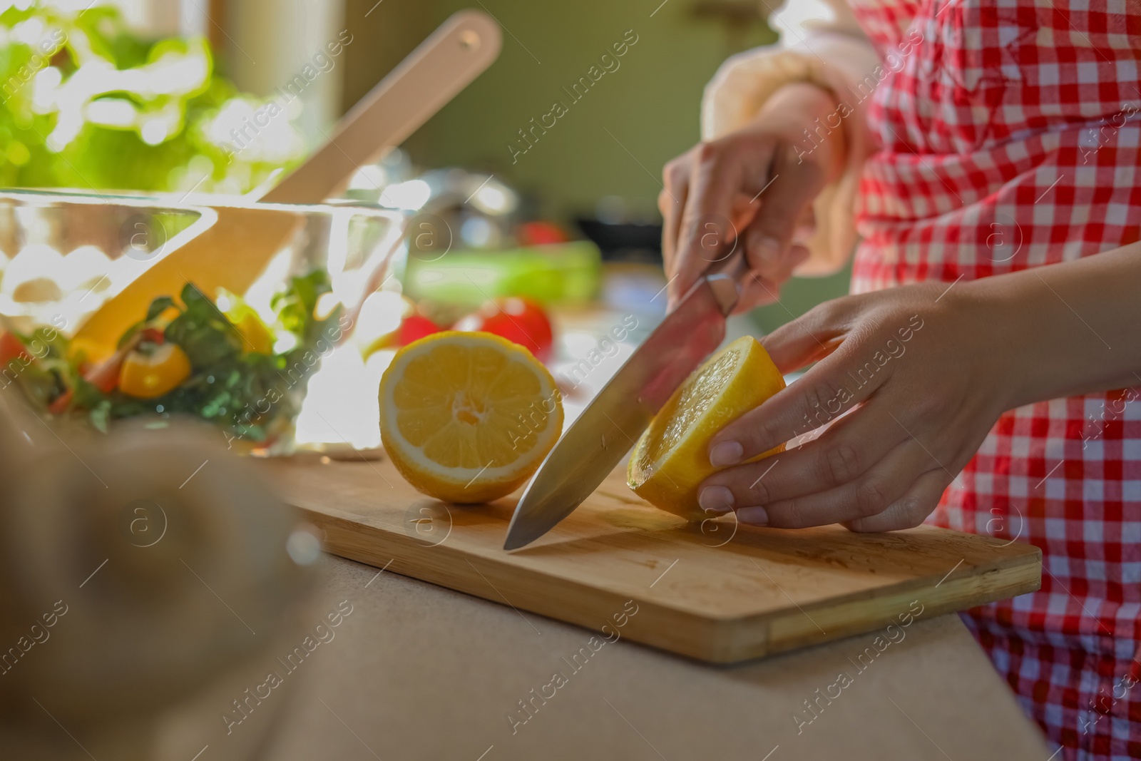 Photo of Woman cutting fresh lemon at countertop in kitchen, closeup