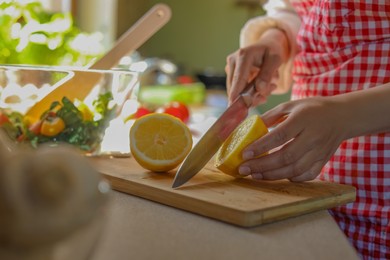 Woman cutting fresh lemon at countertop in kitchen, closeup