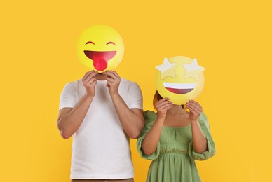 People covering faces with emoticons on yellow background