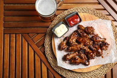 Tasty chicken wings, mug of beer and sauces on wooden table, flat lay with space for text. Delicious snack