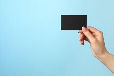 Photo of Woman with blank black business card on light blue background, closeup. Mockup for design
