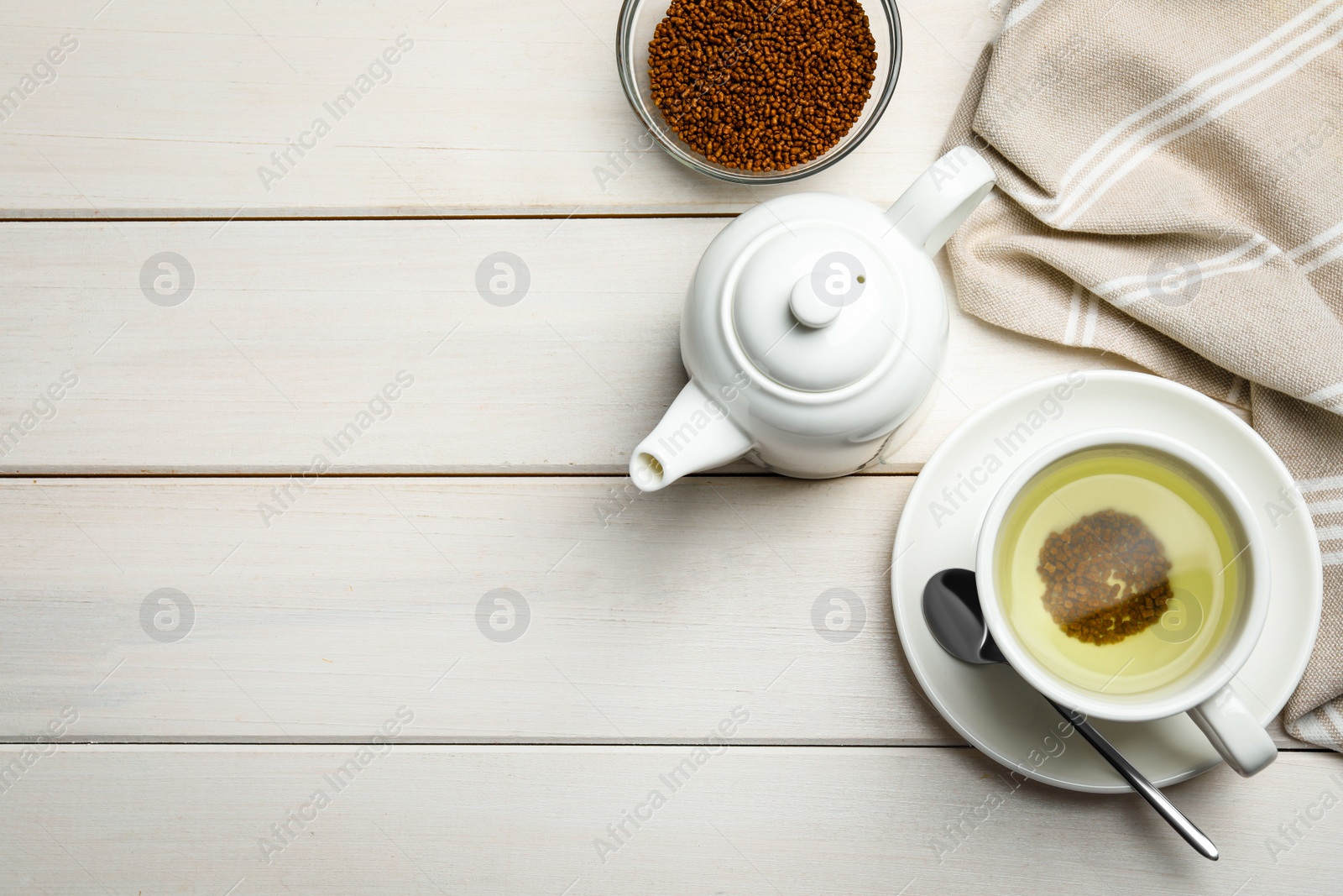 Photo of Cup of buckwheat tea, teapot and granules on white wooden table, flat lay. Space for text
