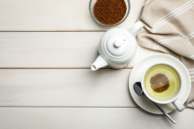Cup of buckwheat tea, teapot and granules on white wooden table, flat lay. Space for text
