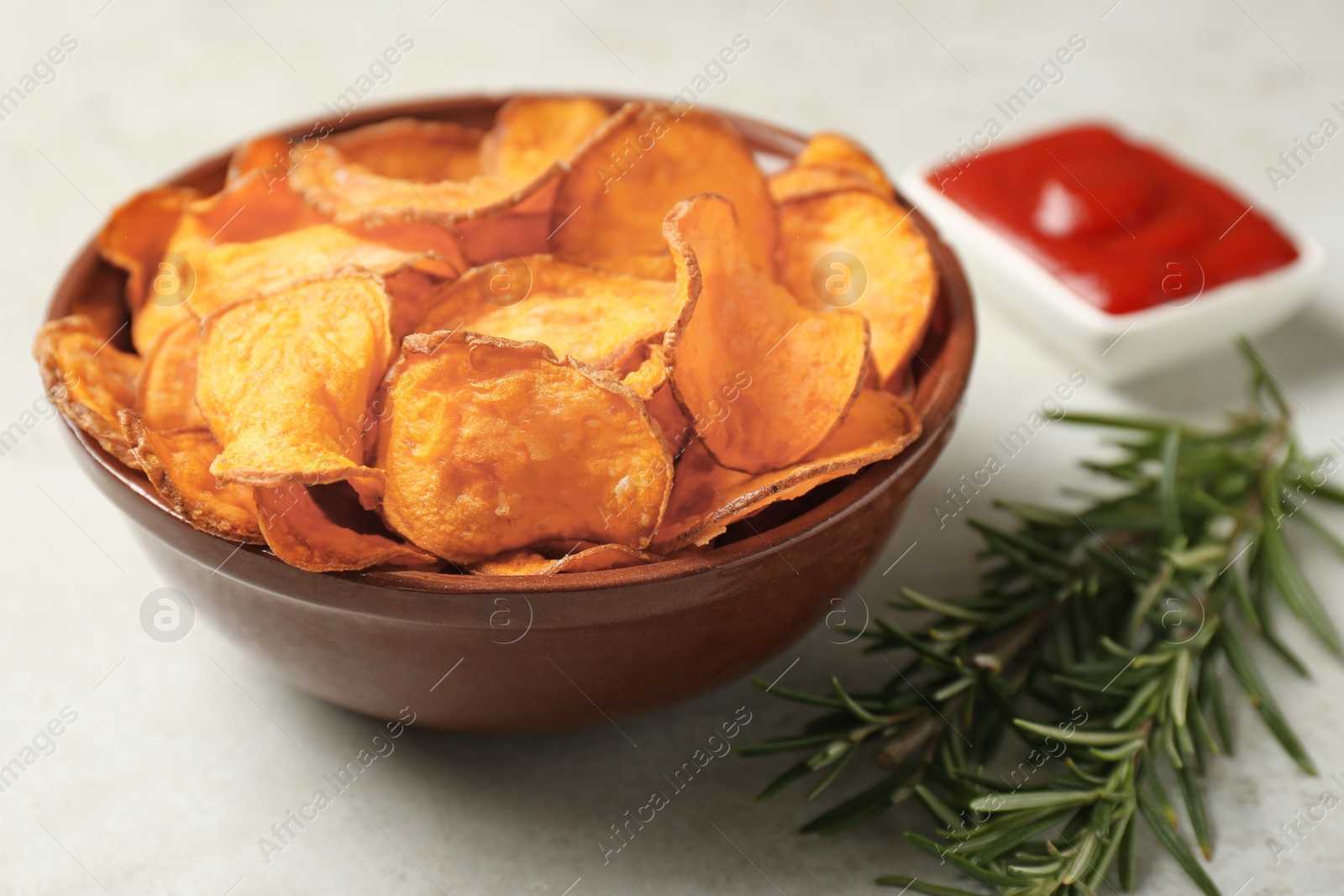 Photo of Delicious sweet potato chips in bowl, rosemary and sauce on table