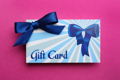 Photo of Gift card with bow on pink background, top view