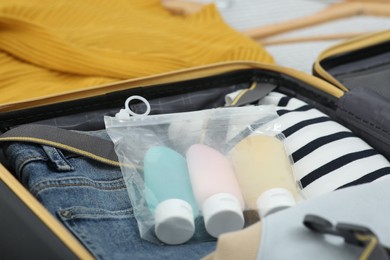 Photo of Plastic bag of cosmetic travel kit and clothes in suitcase. Bath accessories
