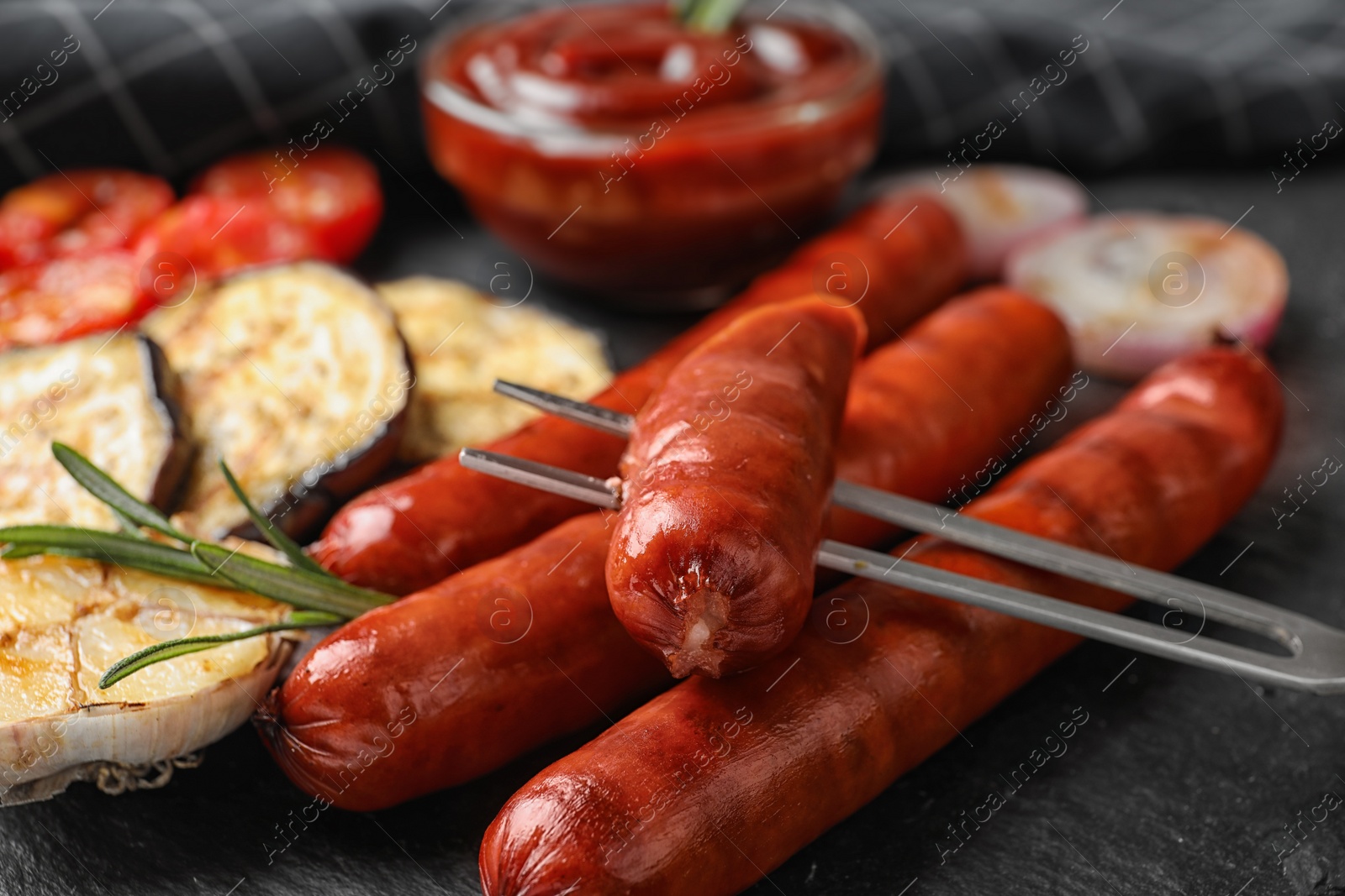 Photo of Delicious grilled sausages and vegetables on black table, closeup. Barbecue food