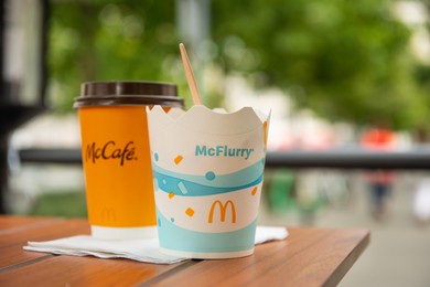 Photo of WARSAW, POLAND - SEPTEMBER 04, 2022: McDonald's hot drink and ice cream on wooden table outdoors, space for text