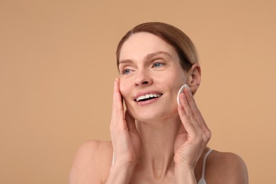 Beautiful woman removing makeup with cotton pad on beige background