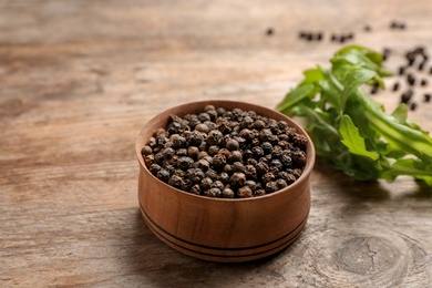 Photo of Bowl with black peppercorns on wooden table