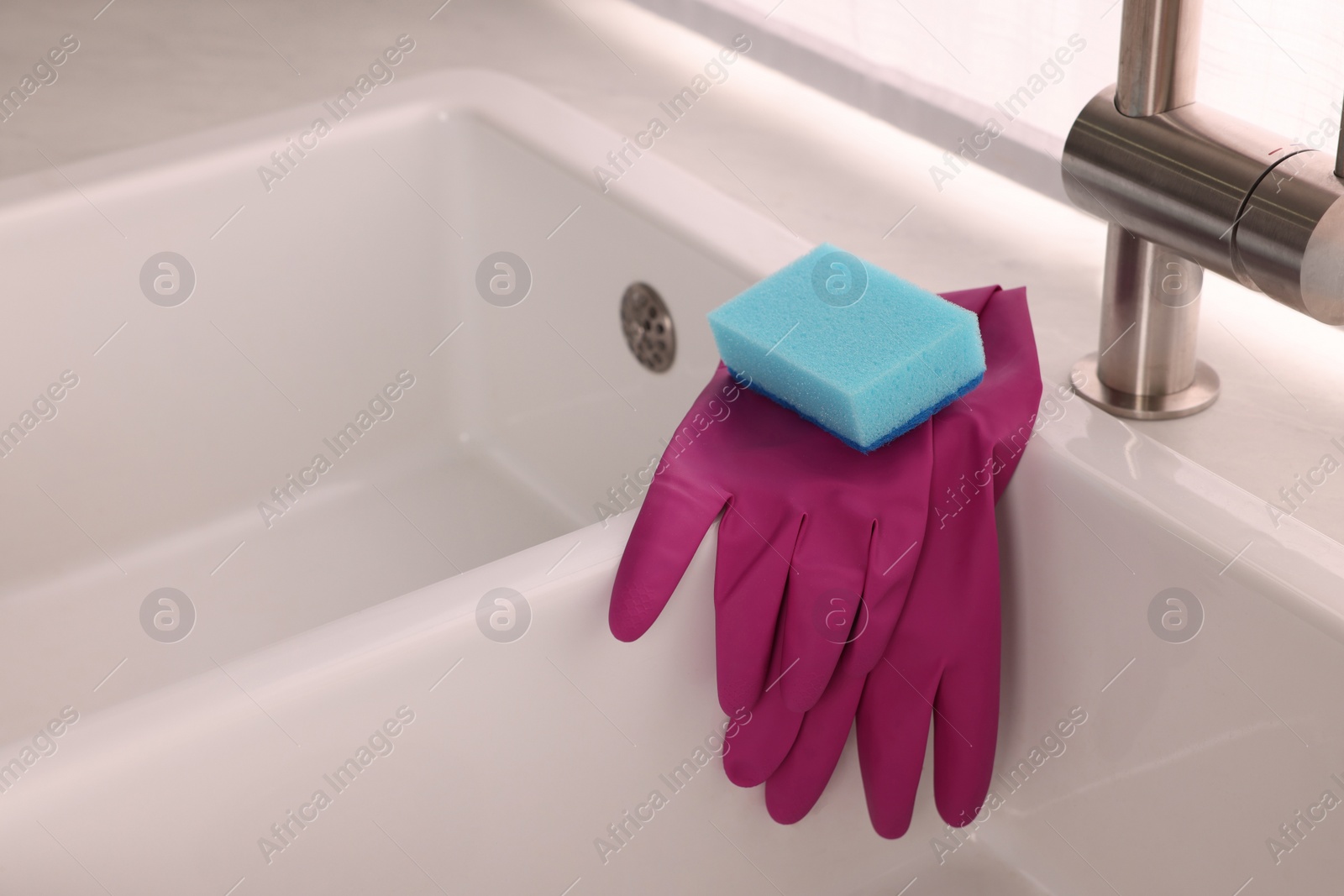 Photo of Sponge and rubber gloves on kitchen sink indoors