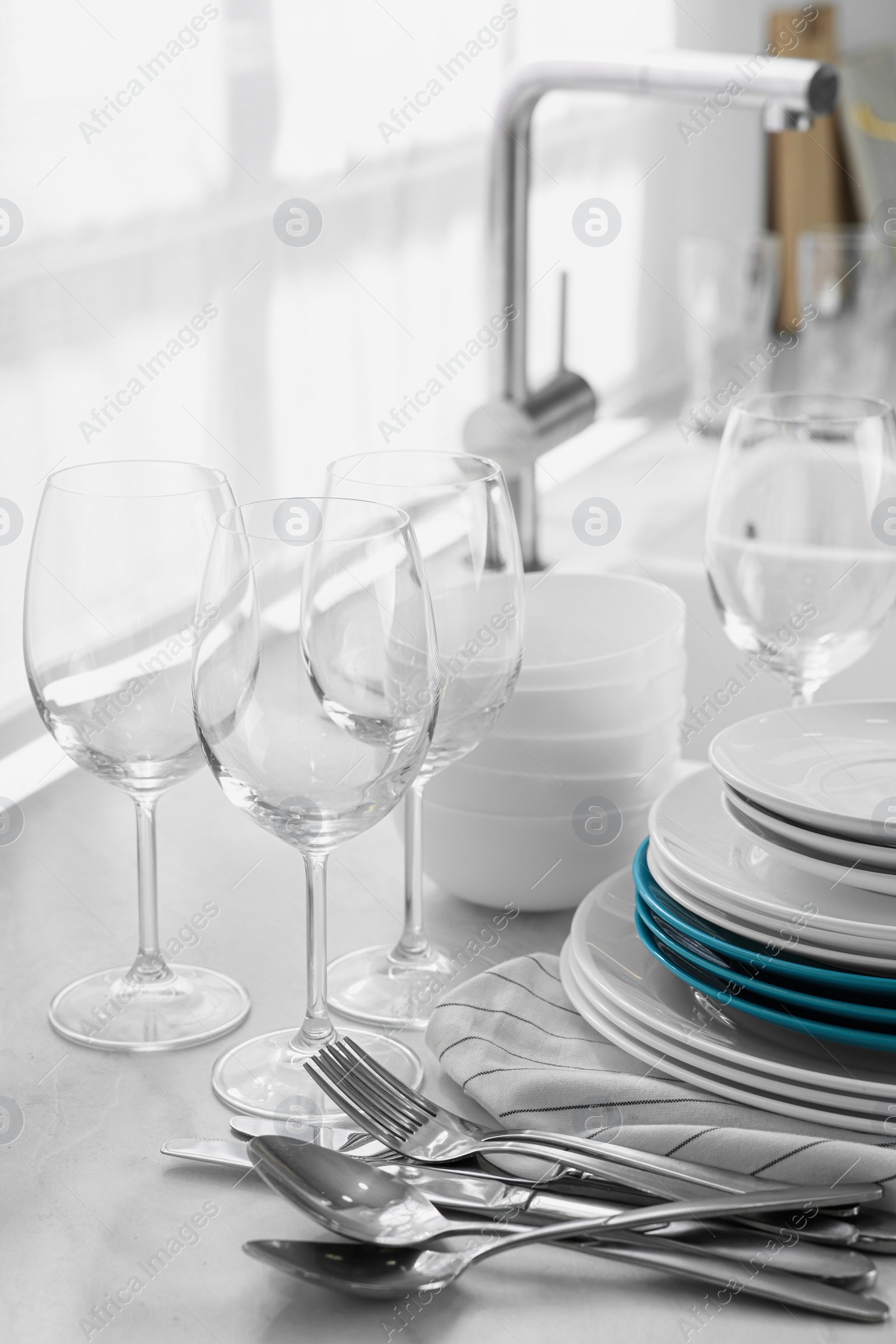 Photo of Different clean dishware, cutlery and glasses on countertop in kitchen