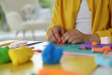 Photo of Little girl sculpting with play dough at table indoors, closeup