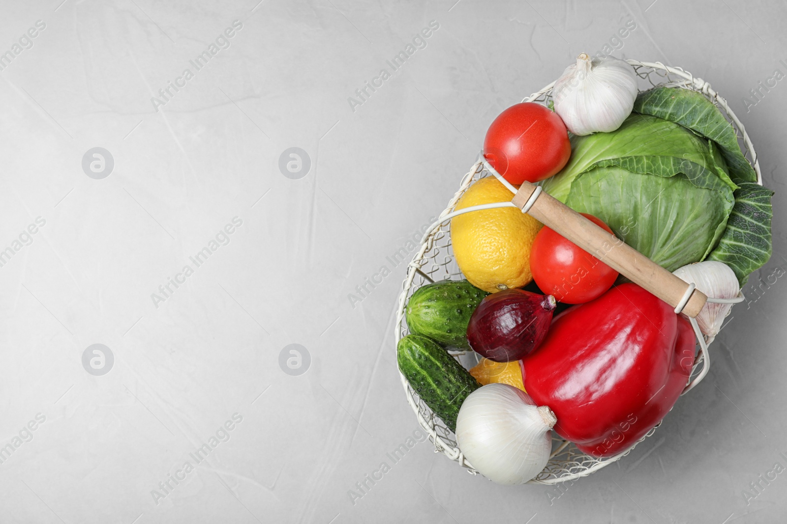 Photo of Basket with ripe fruits and vegetables on light table, top view. Space for text