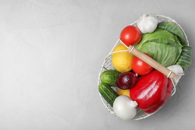 Photo of Basket with ripe fruits and vegetables on light table, top view. Space for text