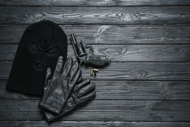 Black knitted balaclava, gloves and gun on grey wooden table, flat lay. Space for text