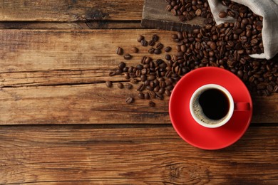 Photo of Cup of aromatic coffee and beans on wooden table, flat lay. Space for text