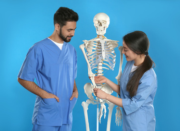 Photo of Young orthopedists with human skeleton model on blue background