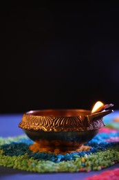 Diwali celebration. Diya lamp and colorful rangoli on table against black background, closeup