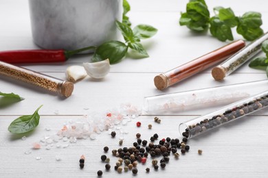 Test tubes with spices, fresh basil leaves, pepper and garlic on white wooden table