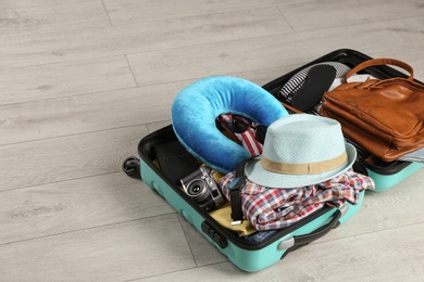 Photo of Opened suitcase with travel pillow and clothes on wooden floor
