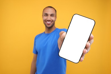 Photo of Young man showing smartphone in hand on yellow background, selective focus. Mockup for design