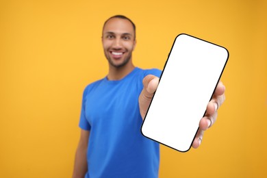 Young man showing smartphone in hand on yellow background, selective focus. Mockup for design