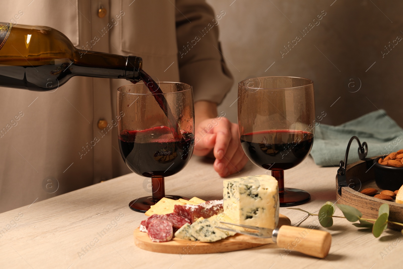 Photo of Woman pouring red wine into glass at wooden table, closeup