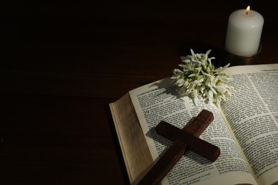Photo of Church candle, Bible, cross and flowers on wooden table, space for text