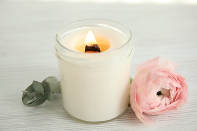 Candle with burning wooden wick and flower on white table