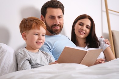 Happy parents with their child reading book on bed at home