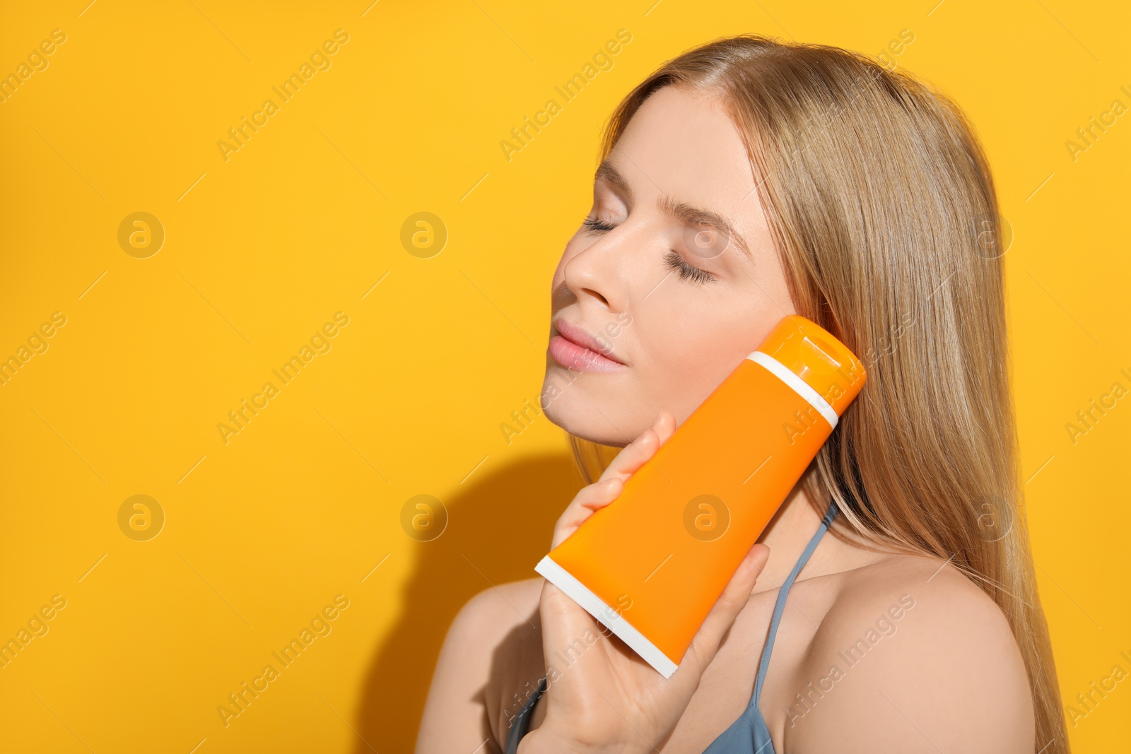 Photo of Beautiful young woman holding sun protection cream on orange background, space for text