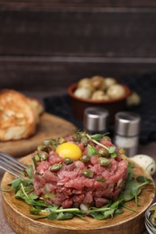 Photo of Tasty beef steak tartare served with yolk, capers and microgreens on serving board