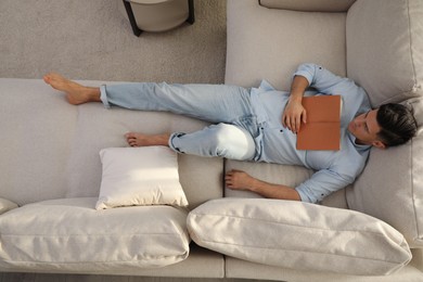 Man with book sleeping on sofa in living room, above view