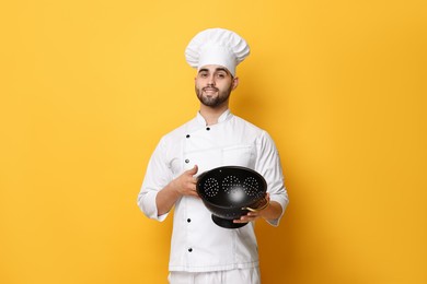 Photo of Professional chef holding colander on yellow background