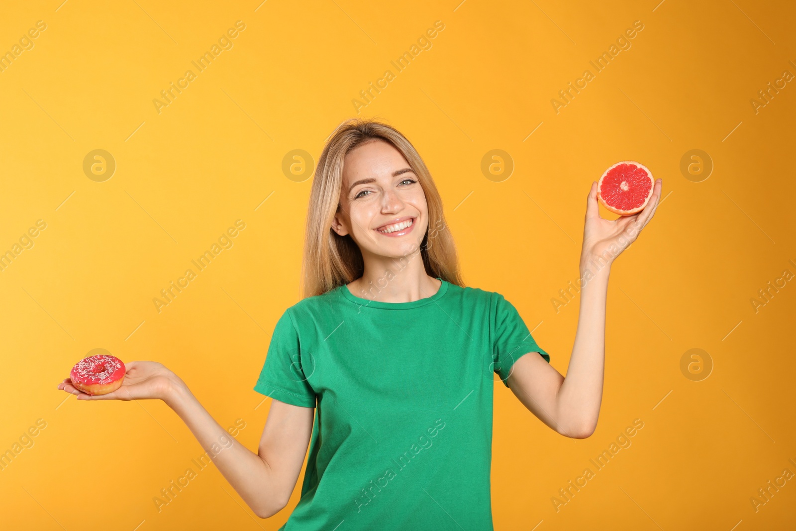 Photo of Woman choosing between doughnut and healthy grapefruit on yellow background