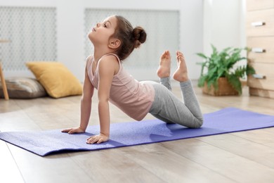 Photo of Little cute girl practicing yoga on mat at home