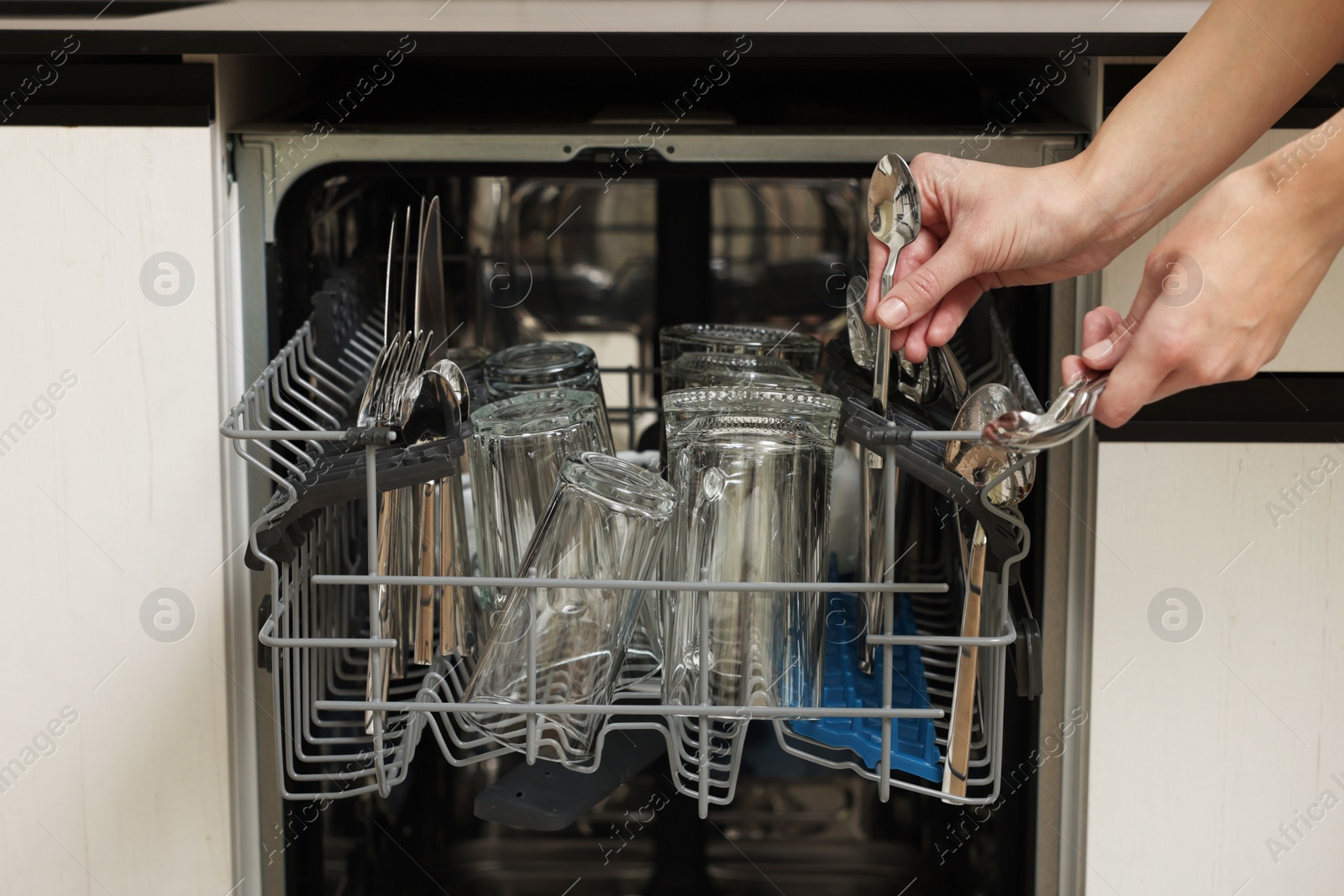 Photo of Woman loading dishwasher with glass and cutlery indoors, closeup