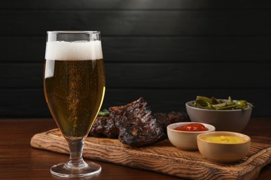 Photo of Glass of beer, delicious grilled ribs and sauces on wooden table