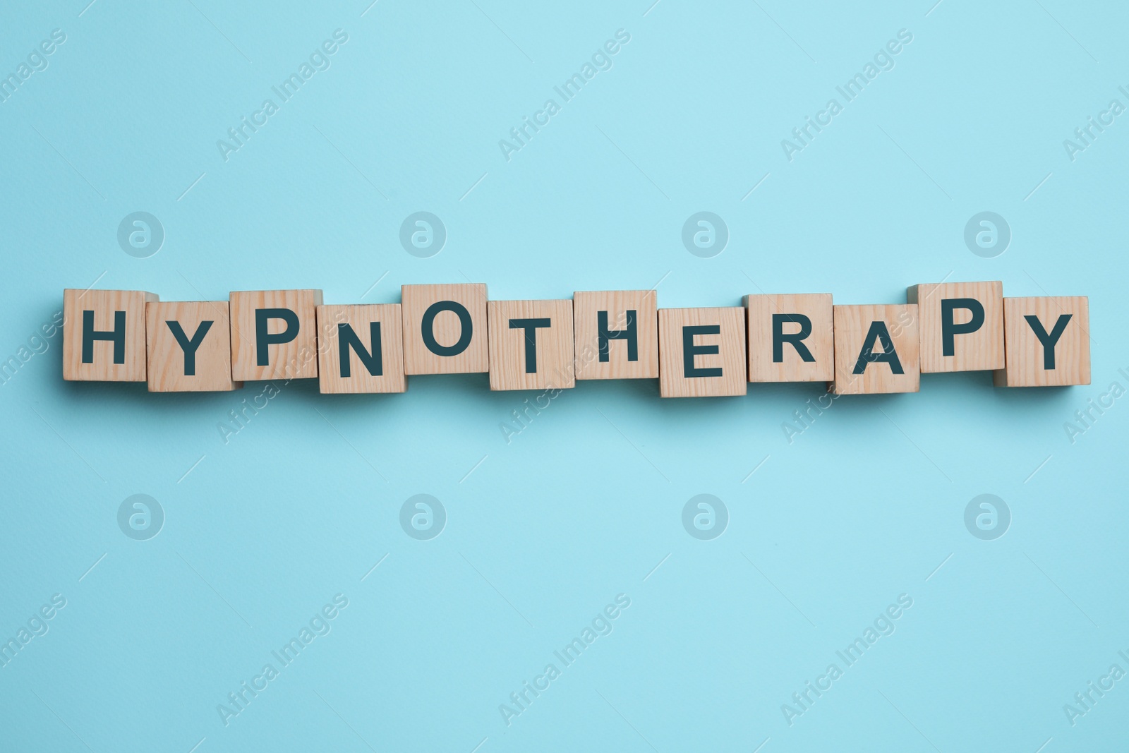 Photo of Wooden blocks with word HYPNOTHERAPY on light blue background, flat lay