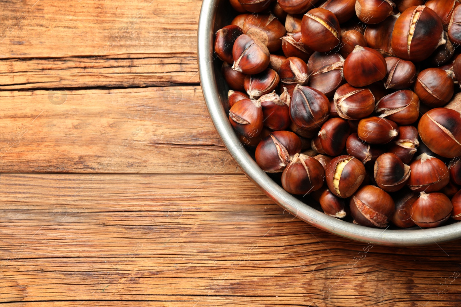 Photo of Delicious roasted edible chestnuts on wooden table, top view. Space for text