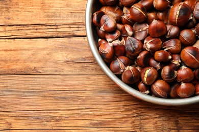 Photo of Delicious roasted edible chestnuts on wooden table, top view. Space for text