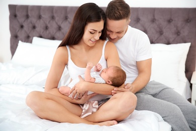 Photo of Happy couple with their newborn baby on bed