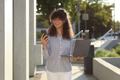 Photo of Happy young woman with modern laptop using smartphone outdoors