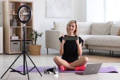 Photo of Smiling sports blogger with with resistance band streaming online fitness lesson at home