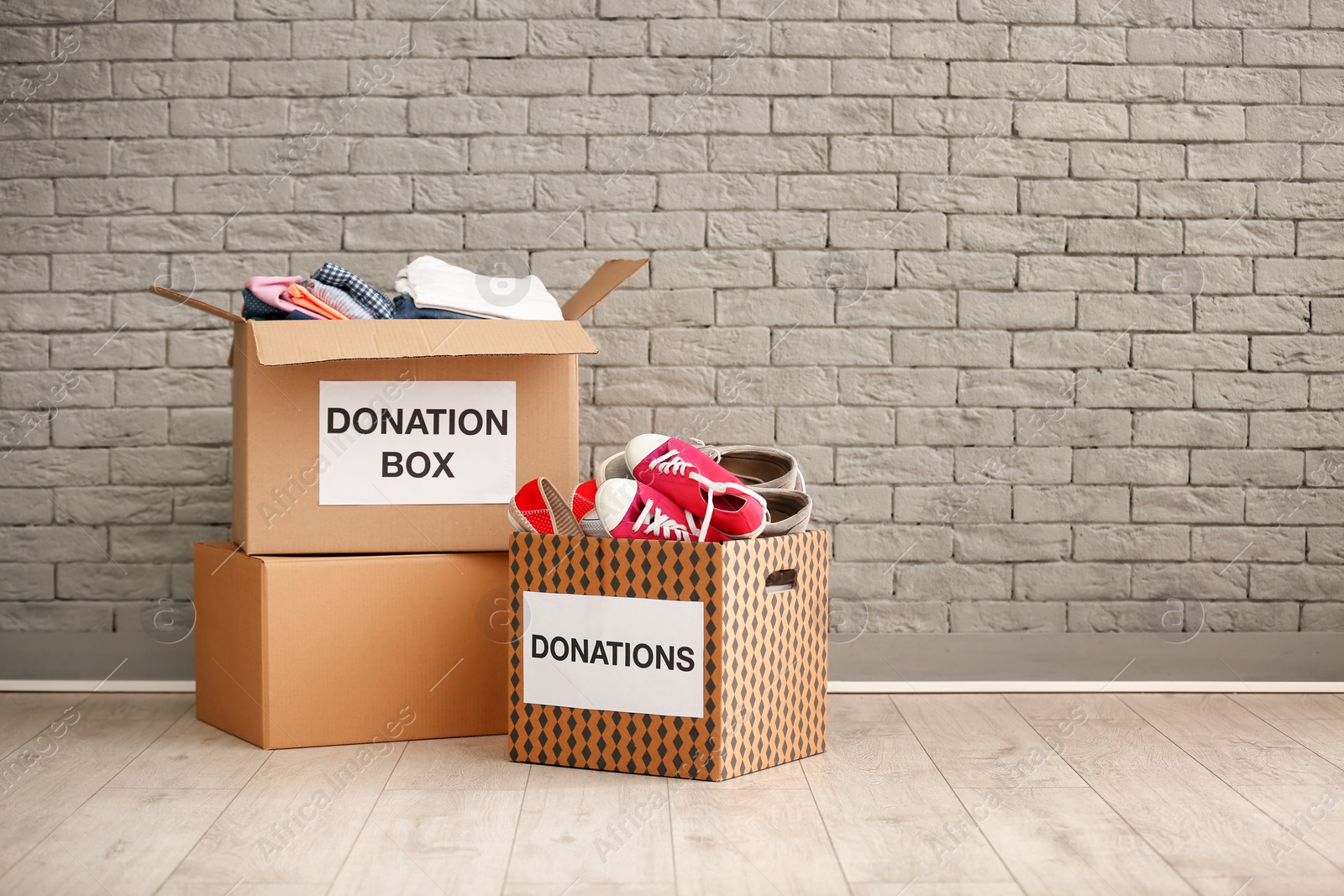 Photo of Donation boxes with clothes and shoes on floor against brick wall