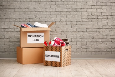 Photo of Donation boxes with clothes and shoes on floor against brick wall